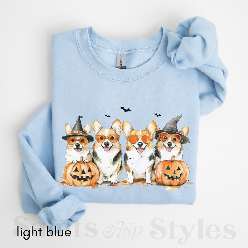May include: Light blue sweatshirt with a graphic of four corgis wearing witch hats and sunglasses, holding pumpkins with jack-o'-lantern faces.