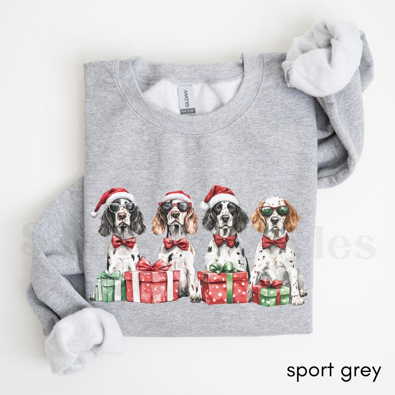 May include: A gray sweatshirt with a Christmas-themed design featuring four dogs wearing Santa hats and sunglasses. The dogs are holding presents wrapped in red and green paper.