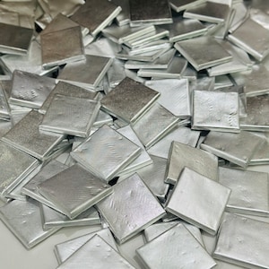 May include: A pile of silver-colored metal squares. The squares are arranged in a random pattern and are all the same size.