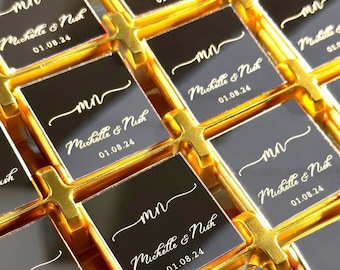 May include: A grid of square black tiles with gold metallic borders. Each tile features the gold printed text "mn" in a script font above the names "Michelle & Nick" and the date "01.08.24" in a clean, elegant typeface, arranged in a repeating pattern.