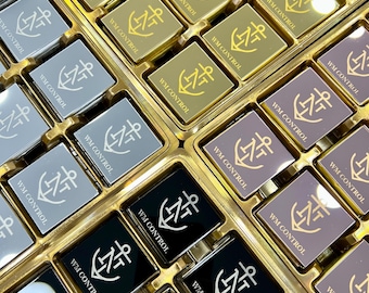 May include: An overhead shot of a tray filled with square, metallic-looking objects. Each square has the text "WM CONTROL" and an anchor symbol. The squares are in various colors, including gold, silver, black, and mauve.