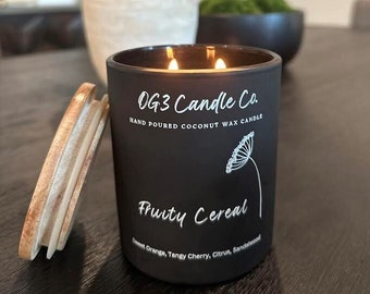Könnte beinhalten: Ein schwarzes Kerzengefäß mit einem weißen Etikett, auf dem "OG3 Candle Co. Hand Poured Coconut Wax Candle Fruity Cereal Sweet Orange, Tangy Cherry, Citrus, Sandalwood" steht.