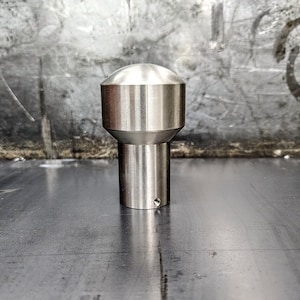 May include: A silver metal knob with a rounded top and a cylindrical base. The knob has a smooth, polished finish.