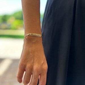 May include: A gold chain bracelet with a nameplate charm. The nameplate is engraved with the word "Kamara".