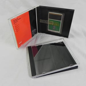 May include: A retro video game cartridge in a clear plastic case. The cartridge is labelled "World Class Baseball" and is set against a black background. The case is open, revealing the game cartridge and an orange and white insert.