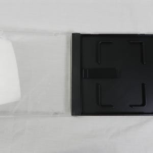 May include: An open, clear plastic CD case with a black tray. The case is rectangular with a hinged design. The black tray has a central hub and four corner clips to hold a CD in place. The case is empty.