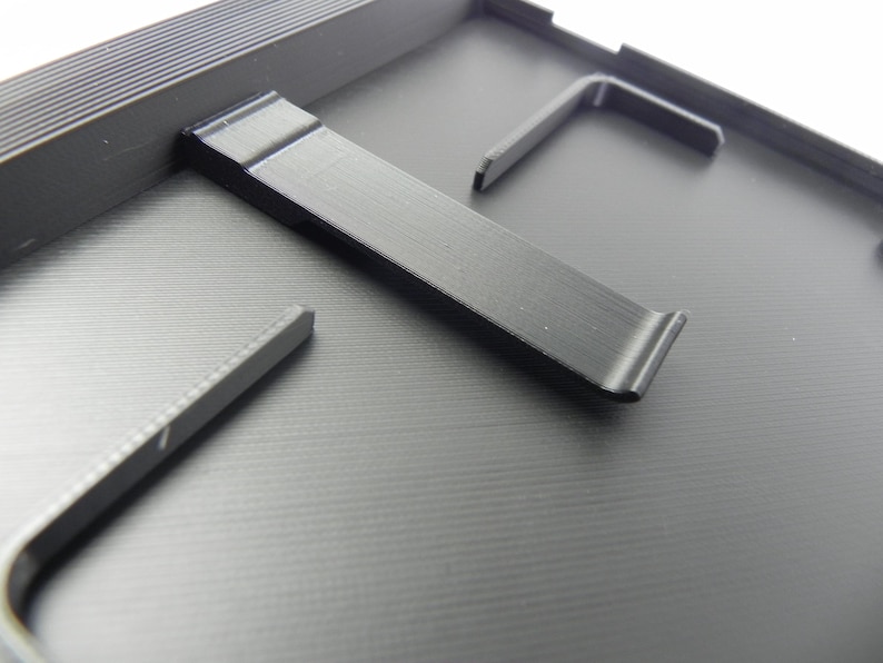 May include: Close-up of a black, textured surface with several black metal components. The components include a long, curved piece and several L-shaped pieces, possibly for assembly or support. The overall aesthetic is industrial and functional.