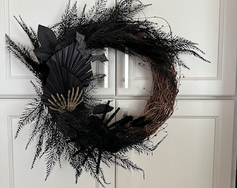 May include: A black and brown Halloween wreath with black feathers, a black fan, and a gold skeleton hand.