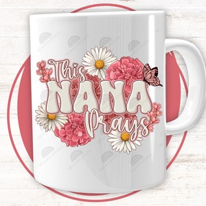 K&ouml;nnte beinhalten: Wei&szlig;e Keramiktasse mit floralem Design und dem Text "This Nana prays".