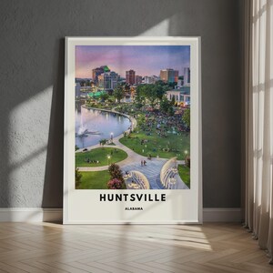 May include: A rectangular wall art print featuring a twilight cityscape of Huntsville, Alabama. The image displays a park with a lake, a fountain, and people gathered on the grass, with city buildings in the background. The text HUNTSVILLE ALABAMA is printed below.