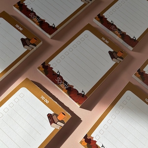 May include: A set of five brown to-do list notepads with an autumnal theme. Each notepad has a white background with lined paper and a decorative border featuring pumpkins, leaves, and a stack of books with a cup of coffee. The text "to do" and "sooty" are printed on each notepad.