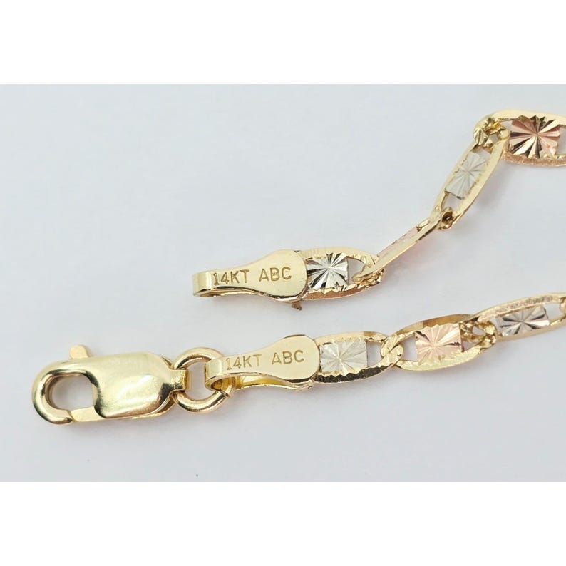 May include: Close-up of a gold chain necklace with a lobster clasp. The chain is made of alternating gold, rose gold, and silver-toned links. The clasp is stamped with "14KT ABC".