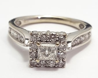 May include: A square-cut diamond ring with a halo of smaller diamonds. The band is white gold with additional diamonds set on each side. The ring is set against a white background.