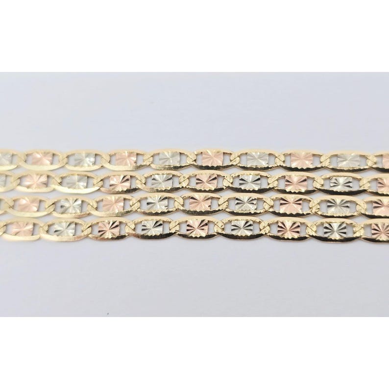 May include: Close-up of three gold-toned chain necklaces. Each chain features an oval link design with starburst-like detailing. The chains are a mix of yellow, white, and rose gold, creating a tricolor effect. The background is plain white.