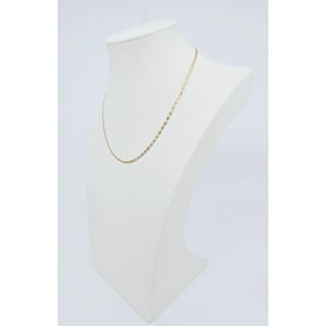 May include: A delicate gold-colored chain necklace displayed on a white mannequin bust. The necklace has a repeating pattern of small, rectangular links. The bust is set against a plain white background, highlighting the jewelry.