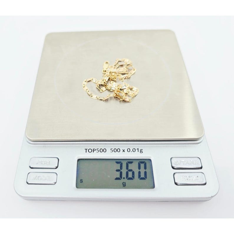 May include: A gold-colored chain necklace rests on a digital scale. The scale displays a weight of 3.60 grams. The scale is silver with the text "TOP500 500 x 0.01g".