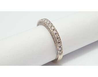 May include: A curved, silver-toned ring with a row of small, clear gemstones. The ring is set against a white background, showcasing its delicate design and sparkling stones. The ring appears to be a wedding band or anniversary ring.