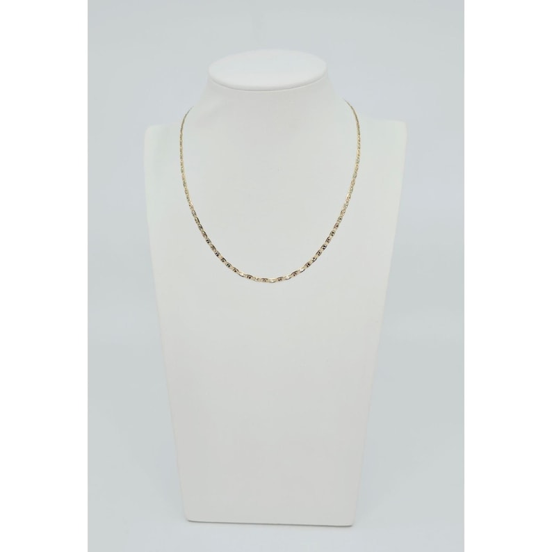 May include: A delicate gold-colored necklace displayed on a white mannequin. The necklace features a fine chain with small, rectangular links. The pendant-free design offers a minimalist and elegant aesthetic, suitable for everyday wear or special occasions.