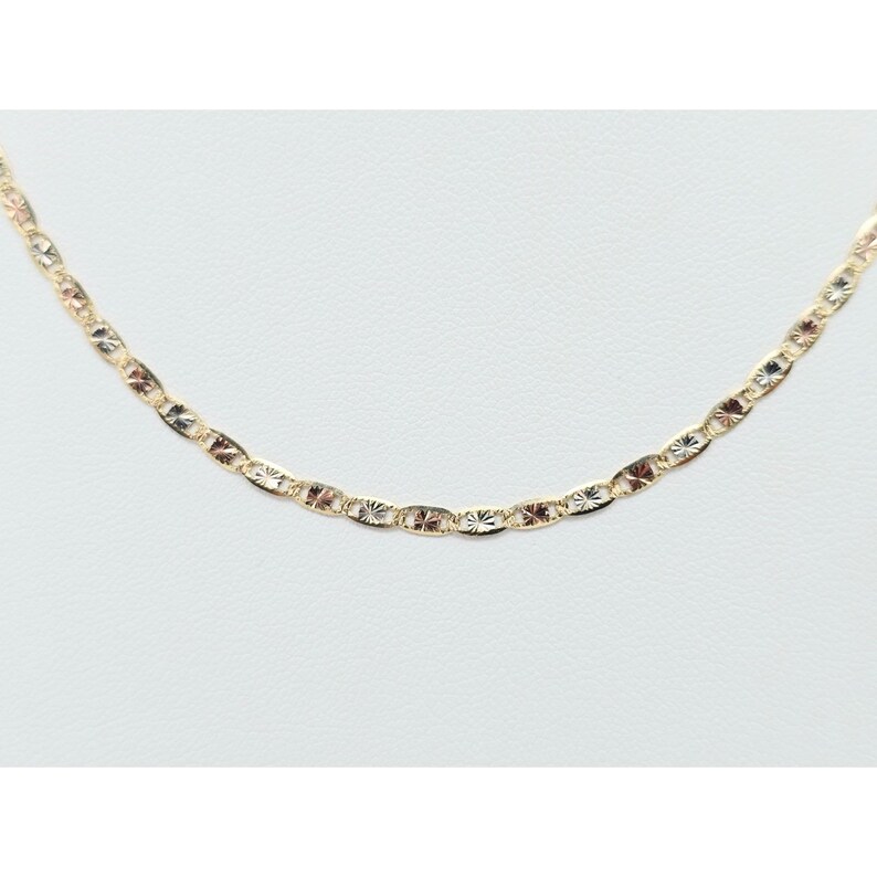 May include: A delicate gold-colored chain necklace with a repeating pattern of oval and star-shaped links. The necklace is displayed on a white background, showcasing its intricate design and subtle shine. The chain is approximately 18 inches long.