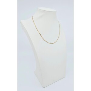 May include: A delicate gold-colored chain necklace displayed on a white mannequin bust. The necklace has a fine, textured design. The bust is set against a plain white background, highlighting the jewelry's details.