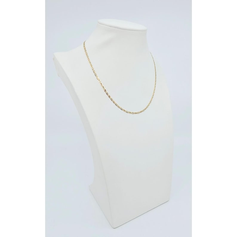 May include: A delicate gold-colored chain necklace displayed on a white mannequin bust. The necklace has a fine, textured design. The bust is set against a plain white background, highlighting the jewelry's details.