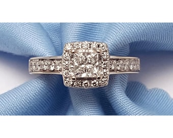 May include: A diamond engagement ring with a square-cut center stone surrounded by a halo of smaller diamonds. The band is also adorned with diamonds. The ring is set on a light blue fabric.