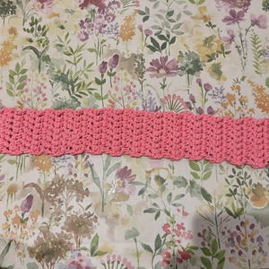 May include: A pink crocheted headband with a scalloped edge.