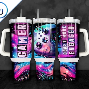 May include: Three insulated travel mugs with white handles and lids. Each mug features a vibrant design with a galaxy theme in shades of blue, purple, and pink. One mug says "GAMER", another has a video game controller, and the third says "BEAST MODE ENGAGED".