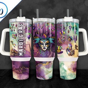 May include: A white travel mug with a purple, green, and gold Mardi Gras themed design. The mug has a handle and a lid with a straw. The text on the mug reads "Mardi Gras - Shut up, liver - you're fine."
