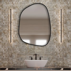 May include: A modern bathroom vanity with a black countertop, a white oval sink, and a black faucet. Above the sink is an irregularly shaped mirror with a black frame. The vanity has a light beige finish with black hardware.
