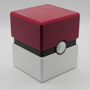 May include: A red and white cube-shaped container with a black band and a white circular button on the side. The top is a solid red, and the bottom is white. The container has a smooth, clean finish.