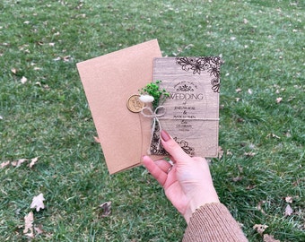 May include: A rustic wooden wedding invitation with a brown envelope. The invitation features a floral design and the text "Wedding of Jenelva Rose & Mark Sitren Celebrate Love Together".