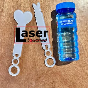 May include: Two white plastic bubble wands with different designs, one shaped like a heart and the other with a bunny head, and a blue bottle of bubble solution labeled "Bubble Blast Solution".