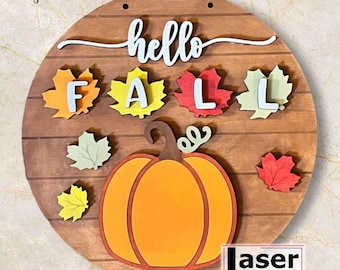 May include: A round wooden sign with the words "hello fall" written in black cursive. The sign is decorated with a pumpkin, leaves, and the letters "FALL" in white. The sign is labeled "Laser touched" in the bottom right corner.