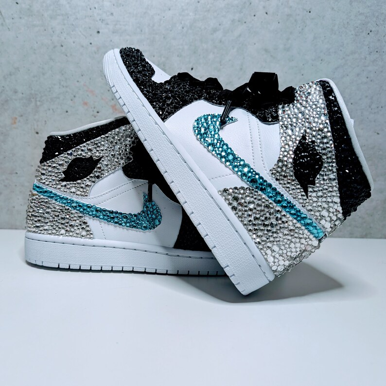 May include: A pair of white high-top sneakers with black and turquoise accents. The sneakers are covered in rhinestones.