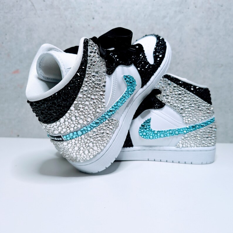 May include: White and black high-top sneakers with a turquoise swoosh and rhinestones covering the entire shoe.