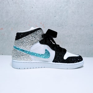 May include: White and black high-top sneakers with a blue swoosh and rhinestones covering the entire shoe.