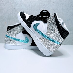 May include: A pair of white and black high-top sneakers with a turquoise swoosh and rhinestones covering the entire shoe.