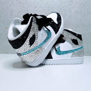 May include: White high-top sneakers with black and blue accents. The sneakers are covered in rhinestones.