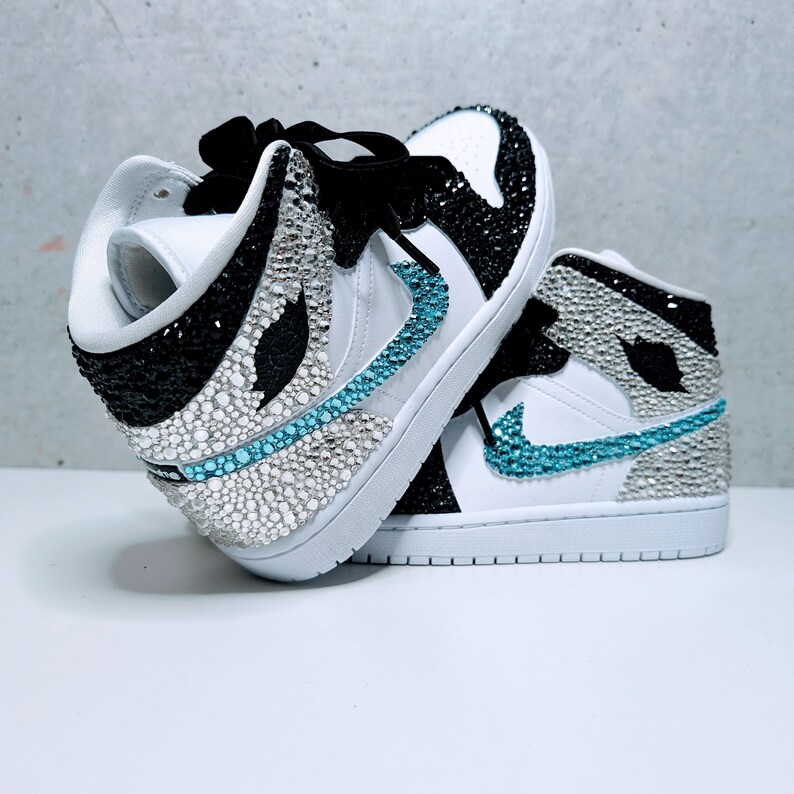 May include: White high-top sneakers with black and blue accents. The sneakers are covered in rhinestones.