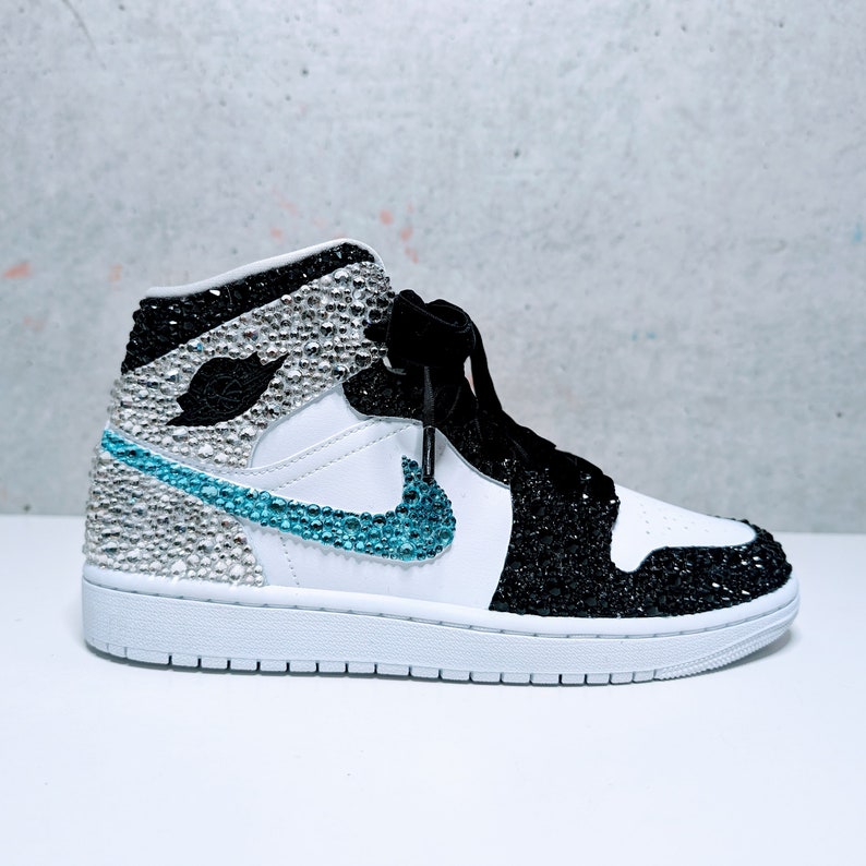 May include: White and black high-top sneakers with a blue swoosh and rhinestones.