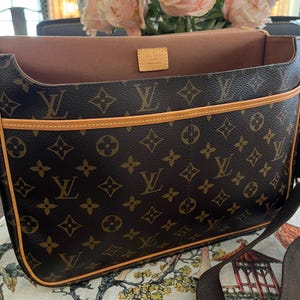 May include: Brown messenger bag with the iconic LV monogram pattern. The bag features a light brown trim and a matching shoulder strap. The interior is a light brown color. A small tag inside the bag reads "Louis Vuitton Paris Made in France."