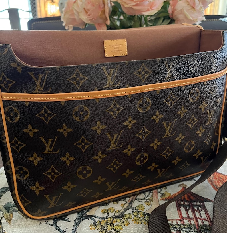 May include: Brown messenger bag with the iconic LV monogram pattern. The bag features a light brown trim and a matching shoulder strap. The interior is a light brown color. A small tag inside the bag reads "Louis Vuitton Paris Made in France."