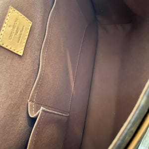 May include: Interior view of a brown handbag with multiple compartments. The bag features a light brown leather tag with the words "LOUIS VUITTON PARIS made in France". The interior is lined with a darker brown fabric.