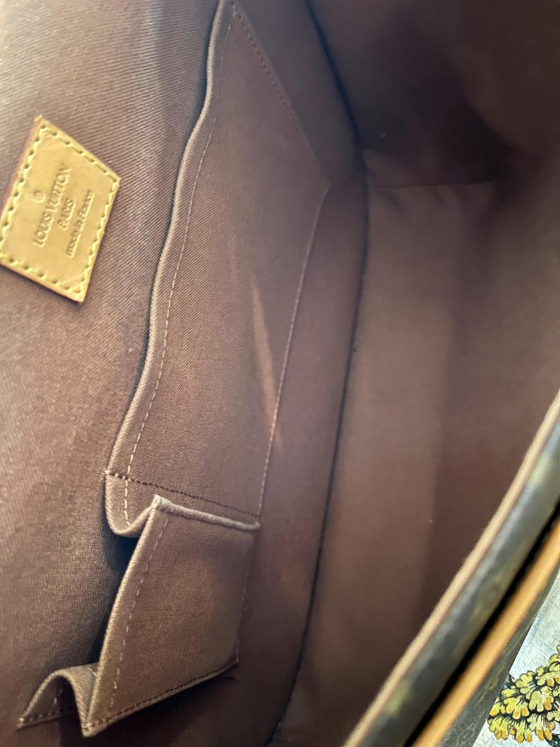 May include: Interior view of a brown handbag with multiple compartments. The bag features a light brown leather tag with the words "LOUIS VUITTON PARIS made in France". The interior is lined with a darker brown fabric.