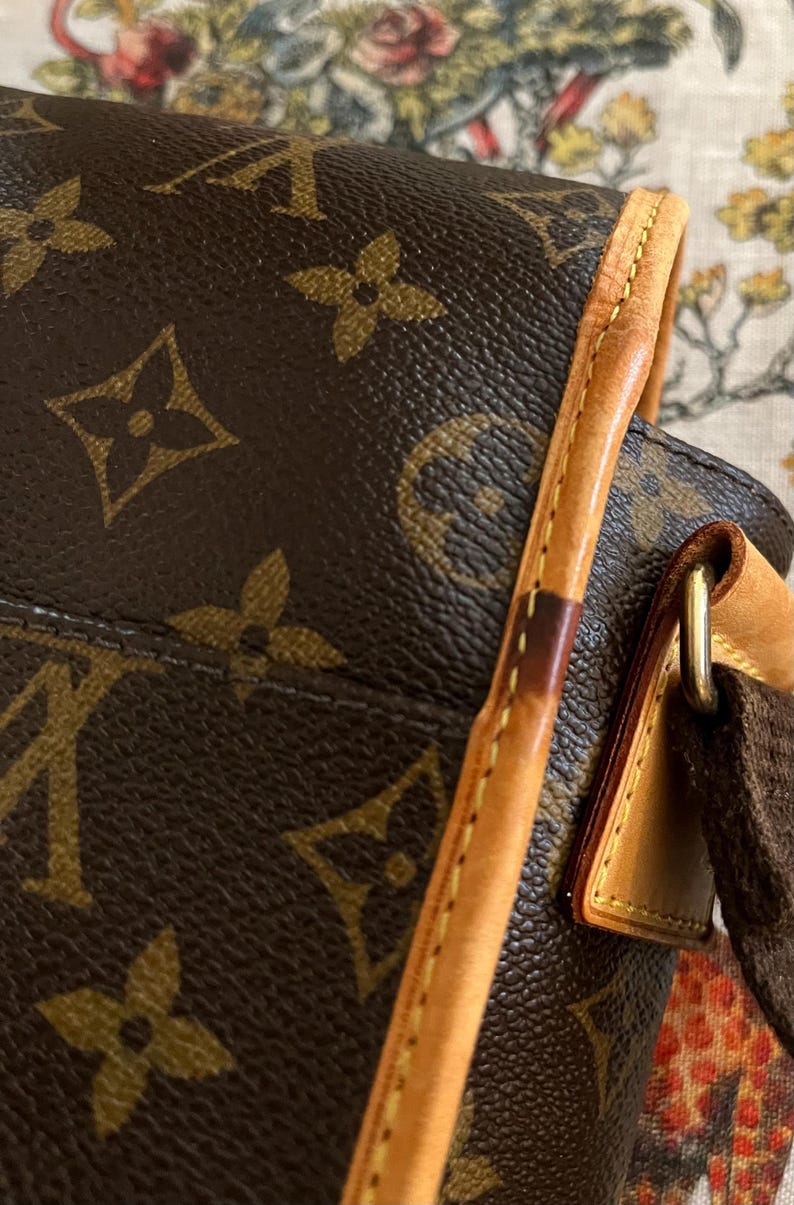 May include: Close-up of a brown leather handbag with the iconic monogram pattern. The bag features a light brown leather trim and a dark brown strap. The stitching is visible along the edges, and the hardware is gold-toned.