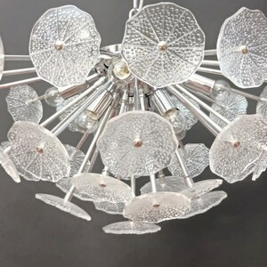 May include: A chrome chandelier with multiple clear glass flower-shaped shades. The chandelier has a modern design and is perfect for a contemporary home.