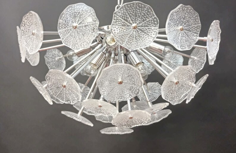 May include: A chrome chandelier with multiple clear glass flower-shaped shades. The chandelier has a modern design and is perfect for a contemporary home.