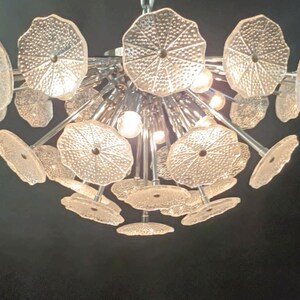 May include: A chrome and glass chandelier with multiple clear glass shades shaped like flower petals. The chandelier has a modern design and is perfect for a contemporary home.