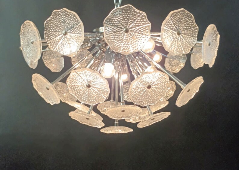 May include: A chrome and glass chandelier with multiple clear glass shades shaped like flower petals. The chandelier has a modern design and is perfect for a contemporary home.